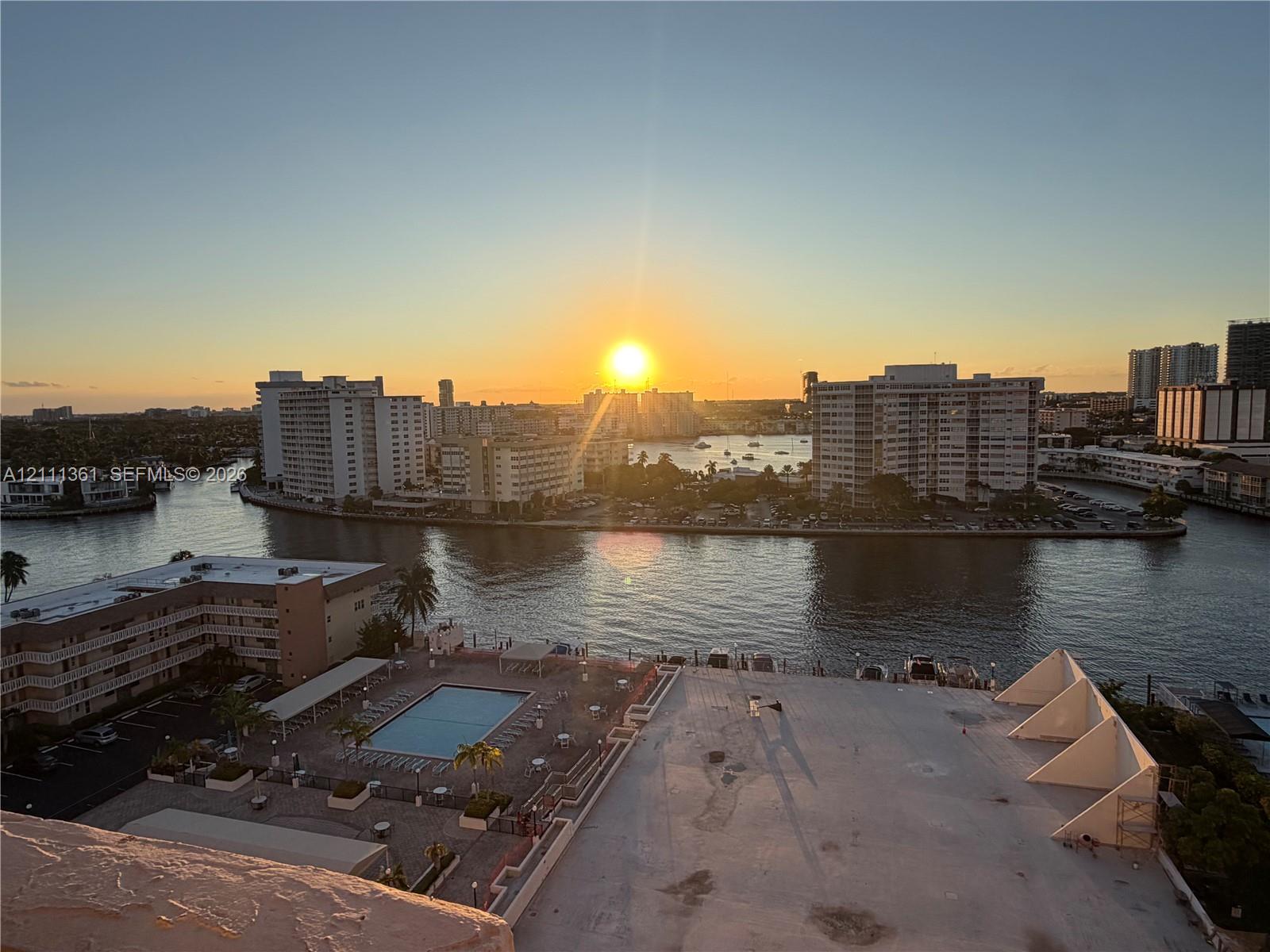 High-rise aerial perspective featuring a swimming pool, paved sundeck, waterway, and sunset horizon