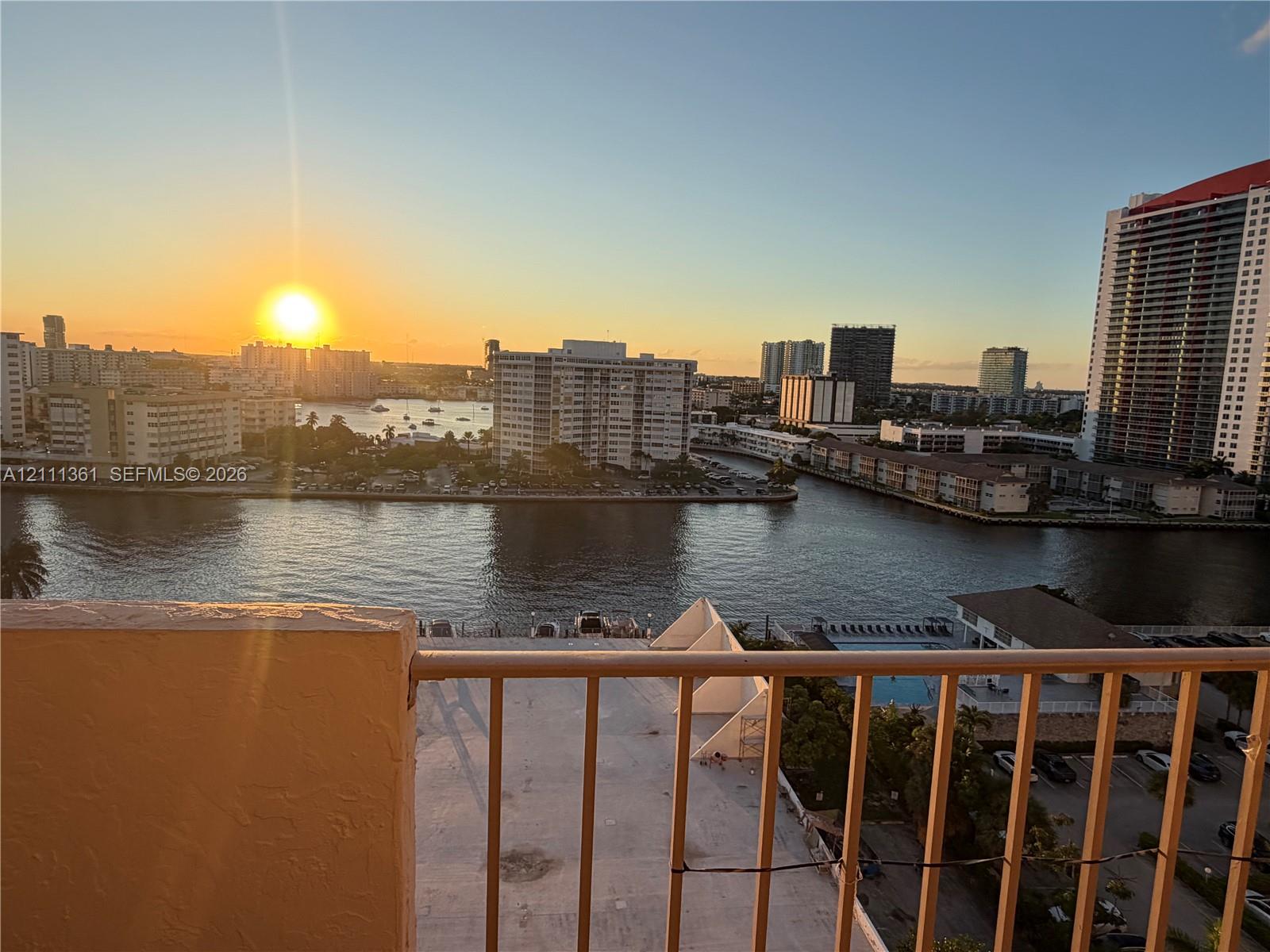Balcony featuring metal railing and expansive water, cityscape, and sunset scenery