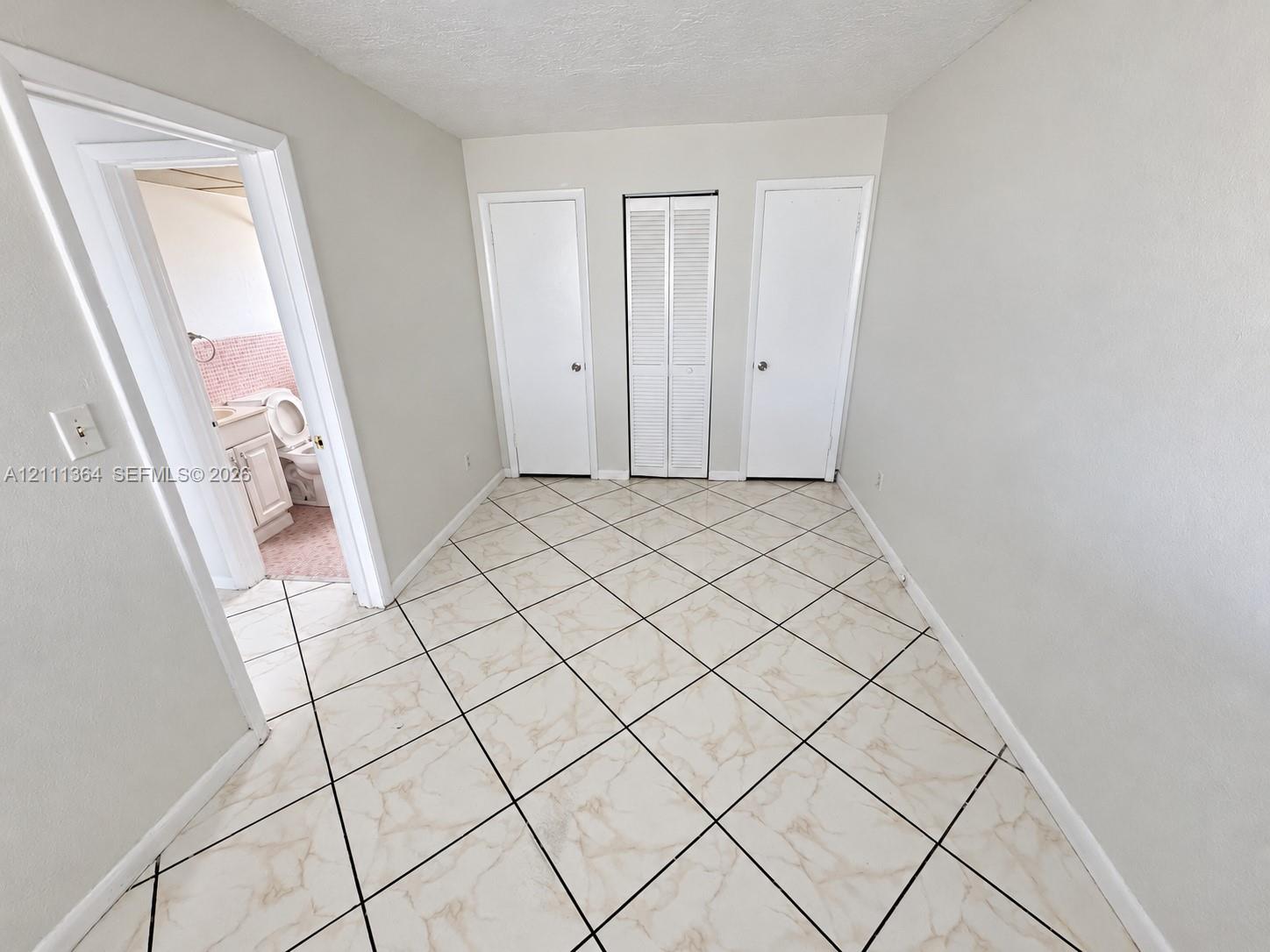Neutral interior space featuring diagonal-set tile flooring, two standard panel doors, and a central louvered-panel closet door
