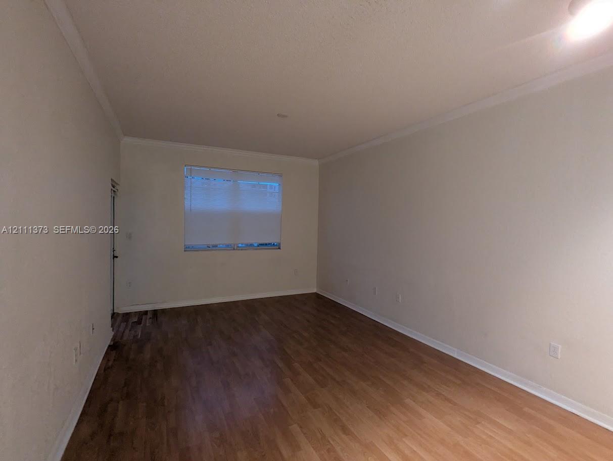 Interior space featuring wood-finish flooring, neutral wall tones, crown molding, and a single window with integrated blinds Interior space featuring wood-finish flooring, neutral wall tones, crown molding, and a single window with integrated blinds