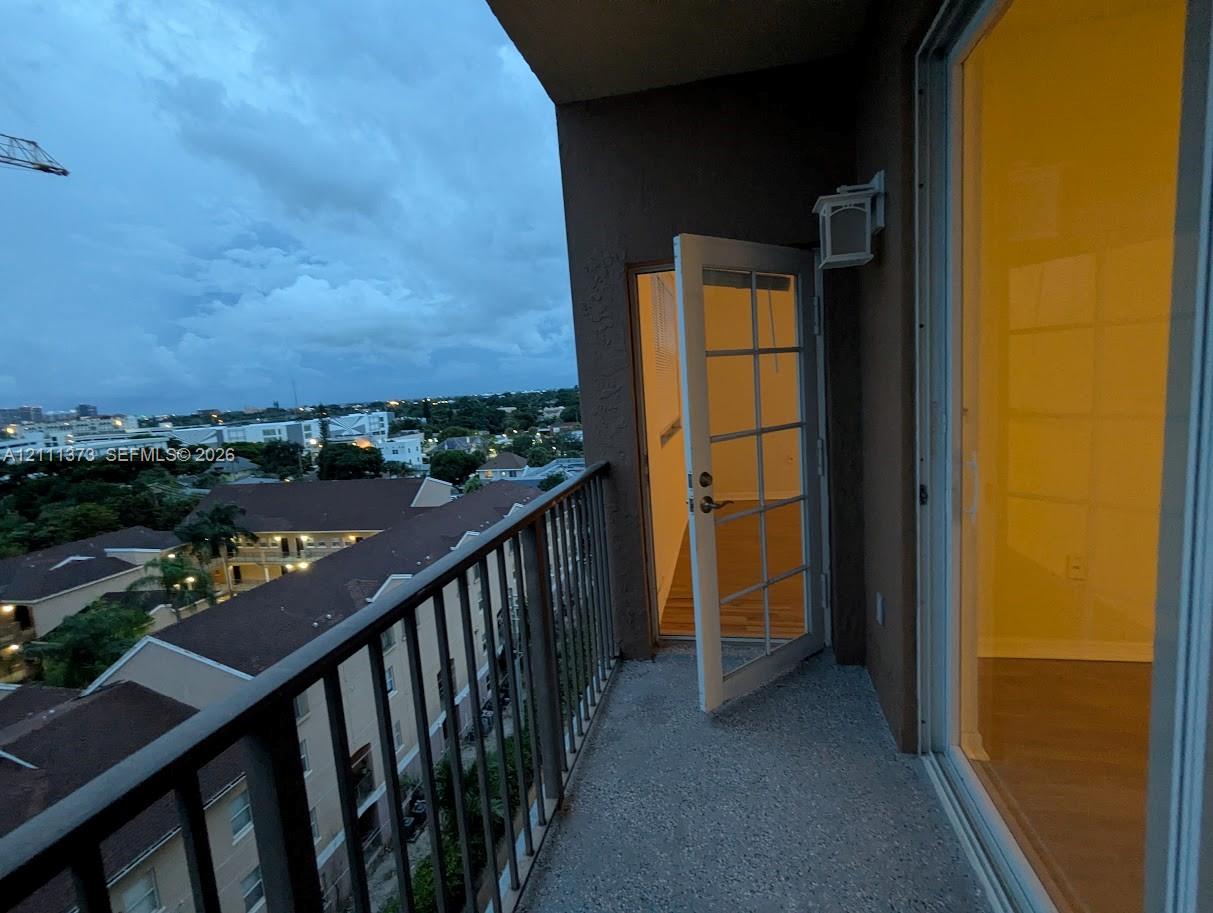 Covered balcony featuring a metal railing, concrete flooring, exterior wall-mounted light fixture, and glass-paned door entry