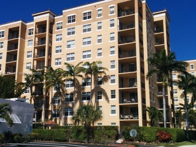 Multi-story residential building featuring stucco facade, recessed private balconies, and landscaped perimeter with mature palm trees Multi-story residential building featuring stucco facade, recessed private balconies, and landscaped perimeter with mature palm trees