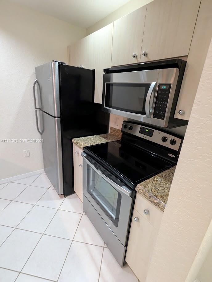 Kitchen featuring light-finish cabinetry, stone-style countertops, stainless steel appliances, and ceramic tile flooring Kitchen featuring light-finish cabinetry, stone-style countertops, stainless steel appliances, and ceramic tile flooring