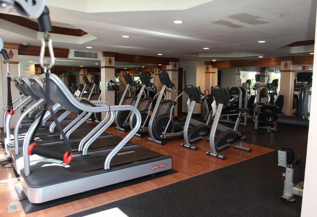 Fitness room featuring mirrored walls, recessed ceiling lighting, wood-finish flooring, and crown molding accents on structural columns