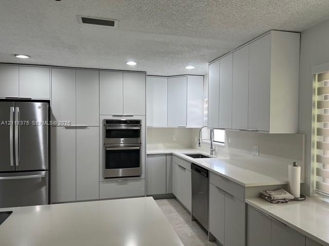 Kitchen featuring custom flat-panel cabinetry, light-toned stone countertops, built-in double wall oven, stainless steel refrigerator, and recessed lighting