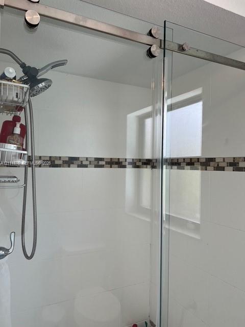 Frameless glass shower enclosure with stainless steel sliding hardware, white wall tile, mosaic tile accent inlay, and adjustable handheld shower head