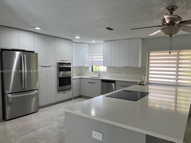 Kitchen featuring white cabinetry, an expansive quartz island with a built-in cooktop, stainless steel appliances including a double wall oven, and large-format tile flooring