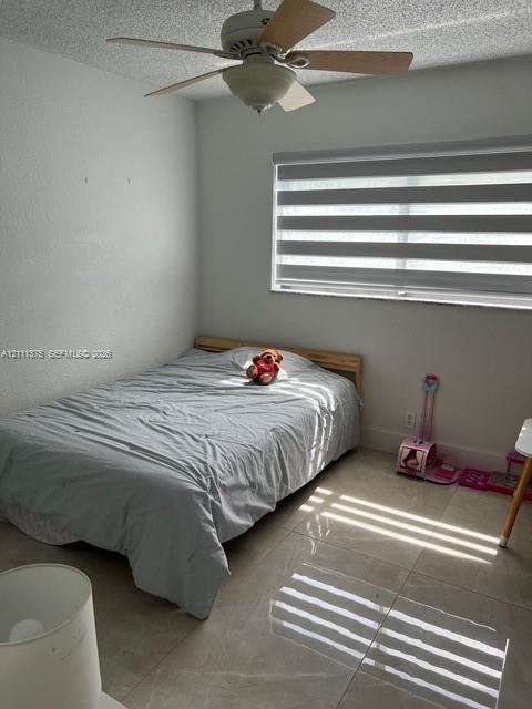 Neutral-toned tile flooring, ceiling fan with light fixture, and horizontal dual-layer window treatments