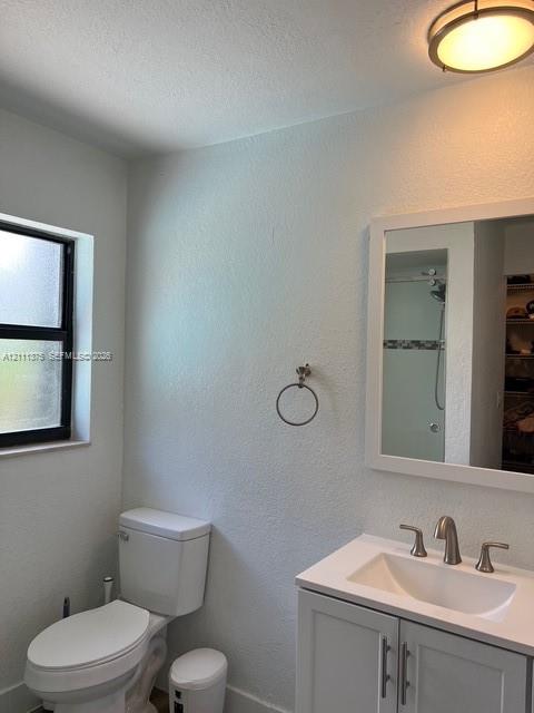White vanity cabinet with integrated countertop and sink, polished metal widespread faucet, framed wall-mounted mirror, round-bowl toilet, and flush-mount ceiling light