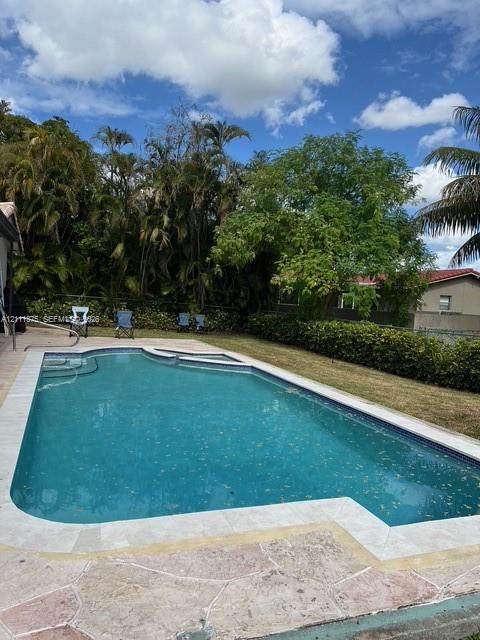 In-ground swimming pool featuring a tile border, stone-finish pool deck, built-in steps, and surrounding mature landscaping