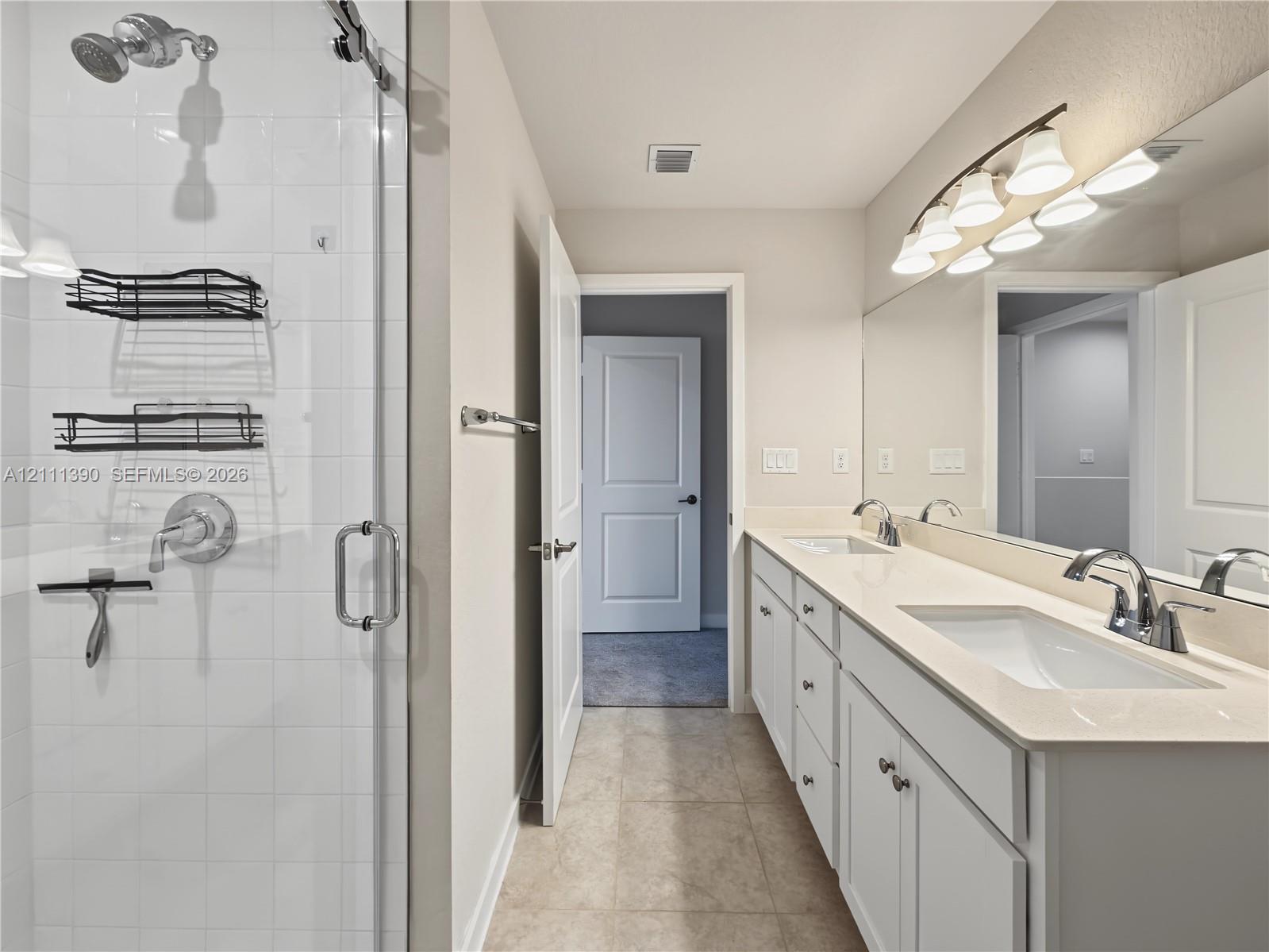 Double vanity featuring a light-toned countertop, rectangular undermount sinks, chrome fixtures, and a multi-bulb vanity light