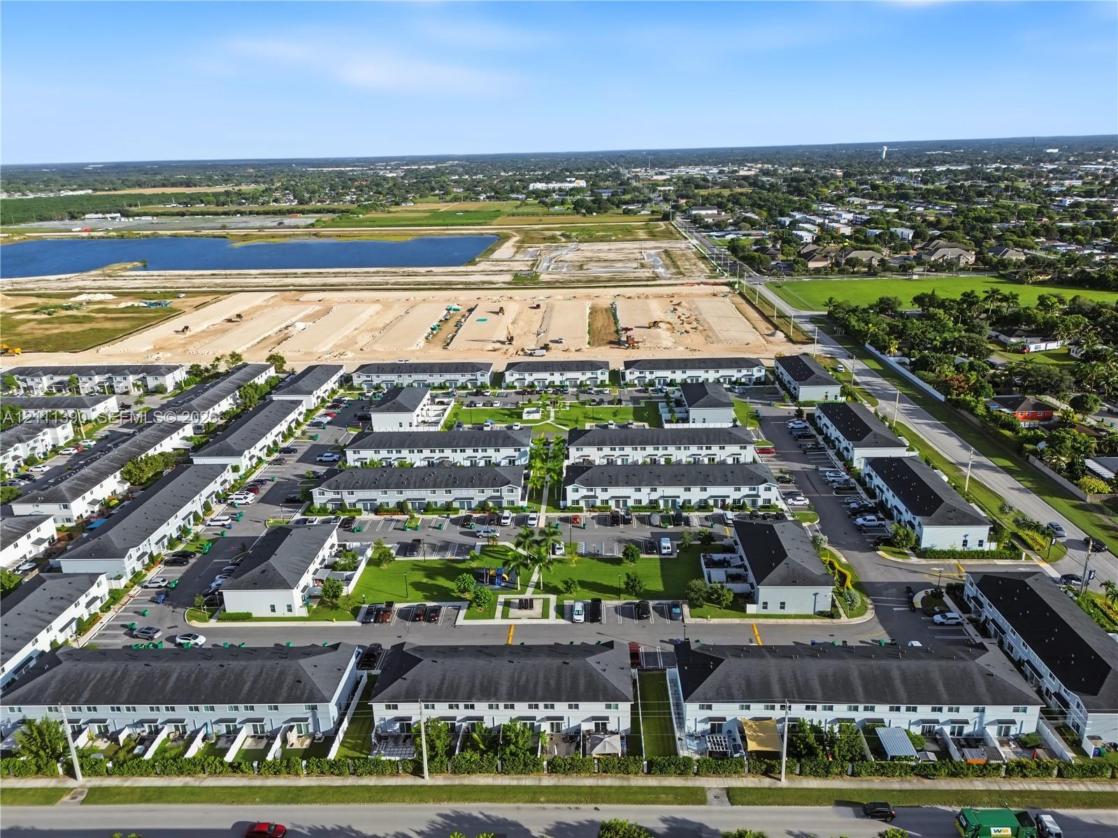 Aerial perspective of a townhome community featuring multi-family residential structures with dark shingled roofs, dedicated surface parking, manicured common green spaces, and perimeter landscaping