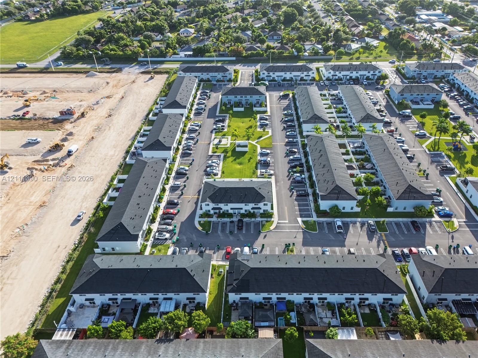 Aerial perspective of multi-family community featuring uniform shingled rooflines, central green space, paved parking areas, and partitioned private outdoor patio sections