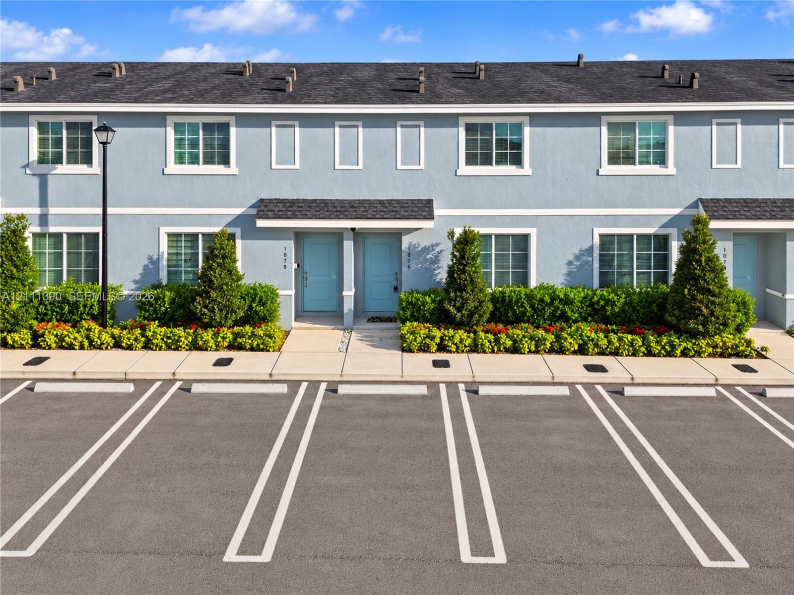 Multi-level exterior featuring light blue siding, dual-tone exterior doors, shingle roofing, and dedicated concrete parking spaces