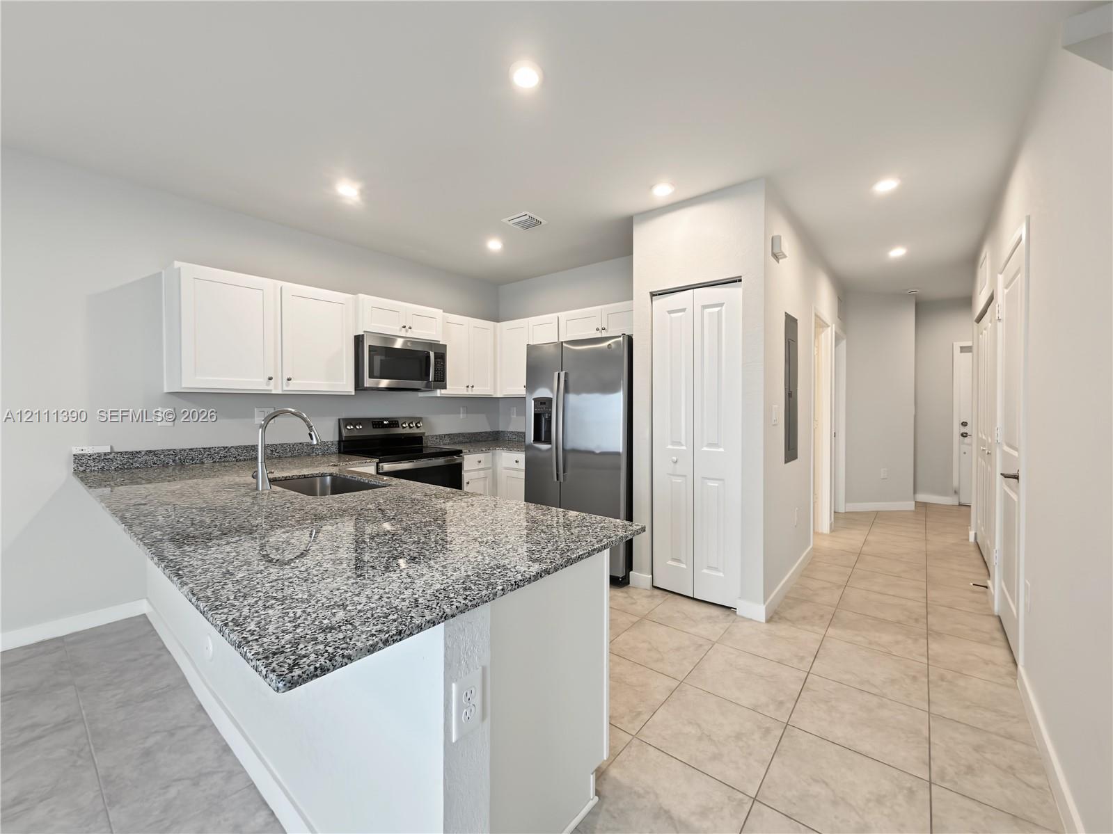 Kitchen featuring a stone countertop peninsula, white shaker-style cabinetry, stainless steel appliances, and tile flooring