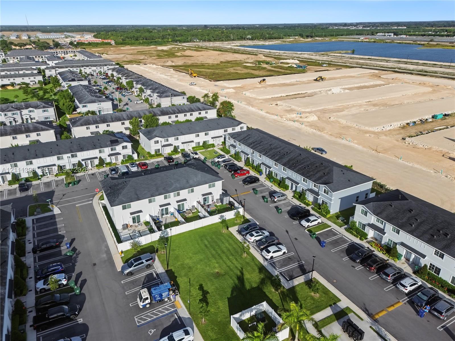 Aerial perspective of a multi-unit residential community featuring light-colored exterior siding, dark shingle roofing, designated paved parking spaces, and manicured green space