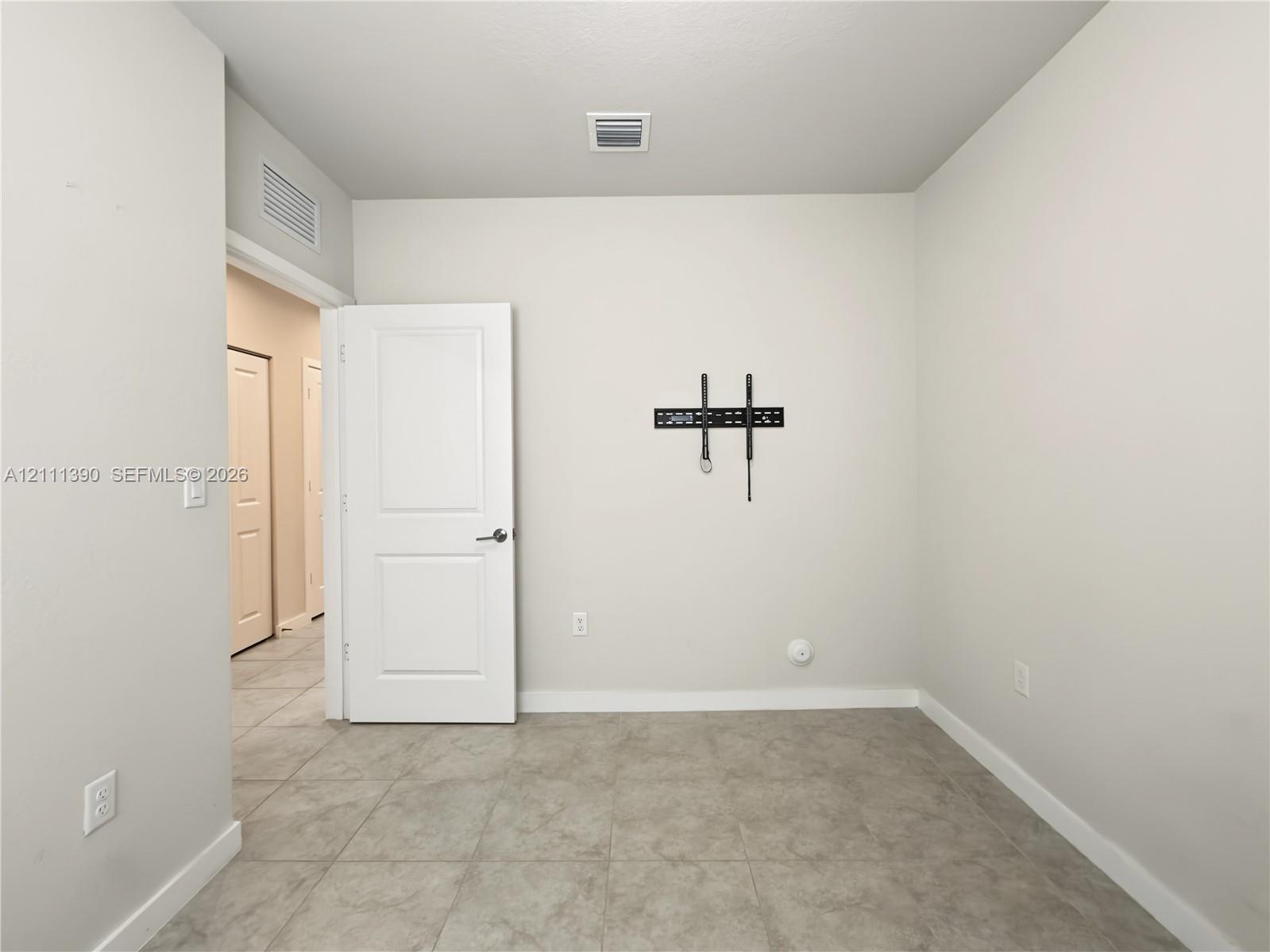 Neutral-toned interior space featuring light-colored tile flooring, smooth wall finishes, a solid-core interior door, and a wall-mounted display bracket