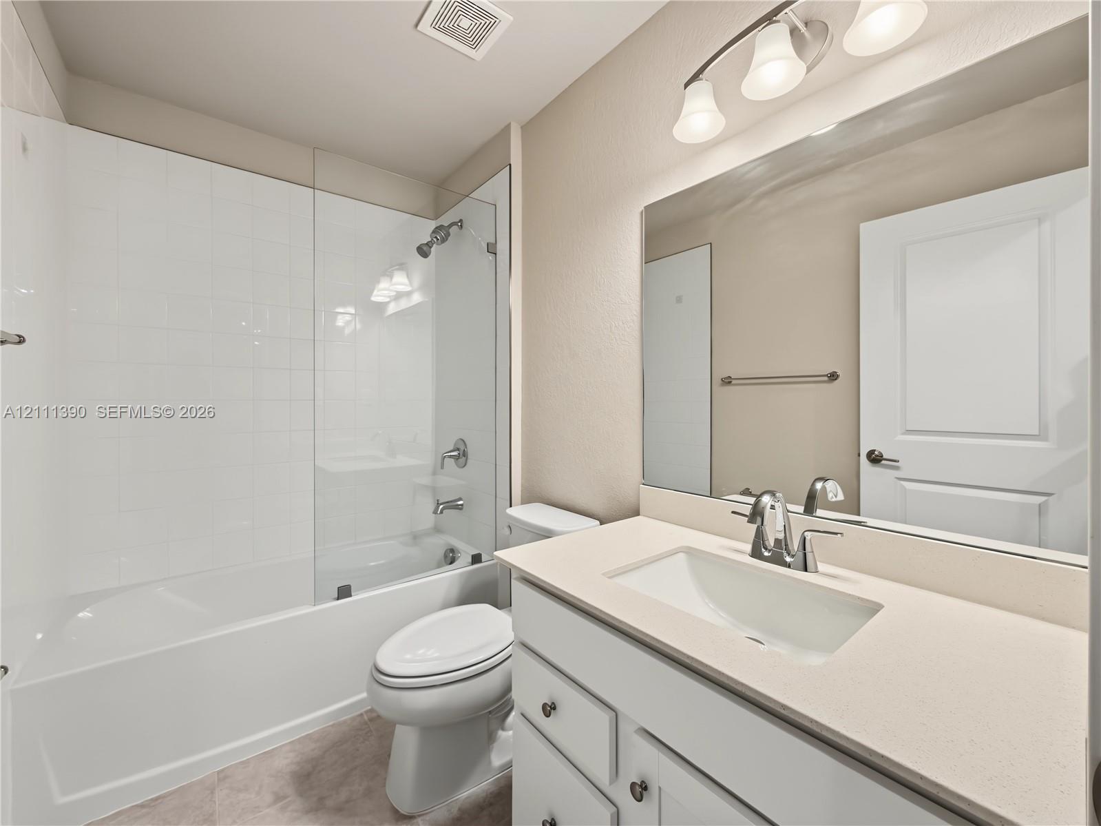 Bathroom featuring a white vanity cabinet with a quartz countertop, an integrated rectangular sink, a large wall-mounted mirror, and a shower-tub combination with a glass panel enclosure