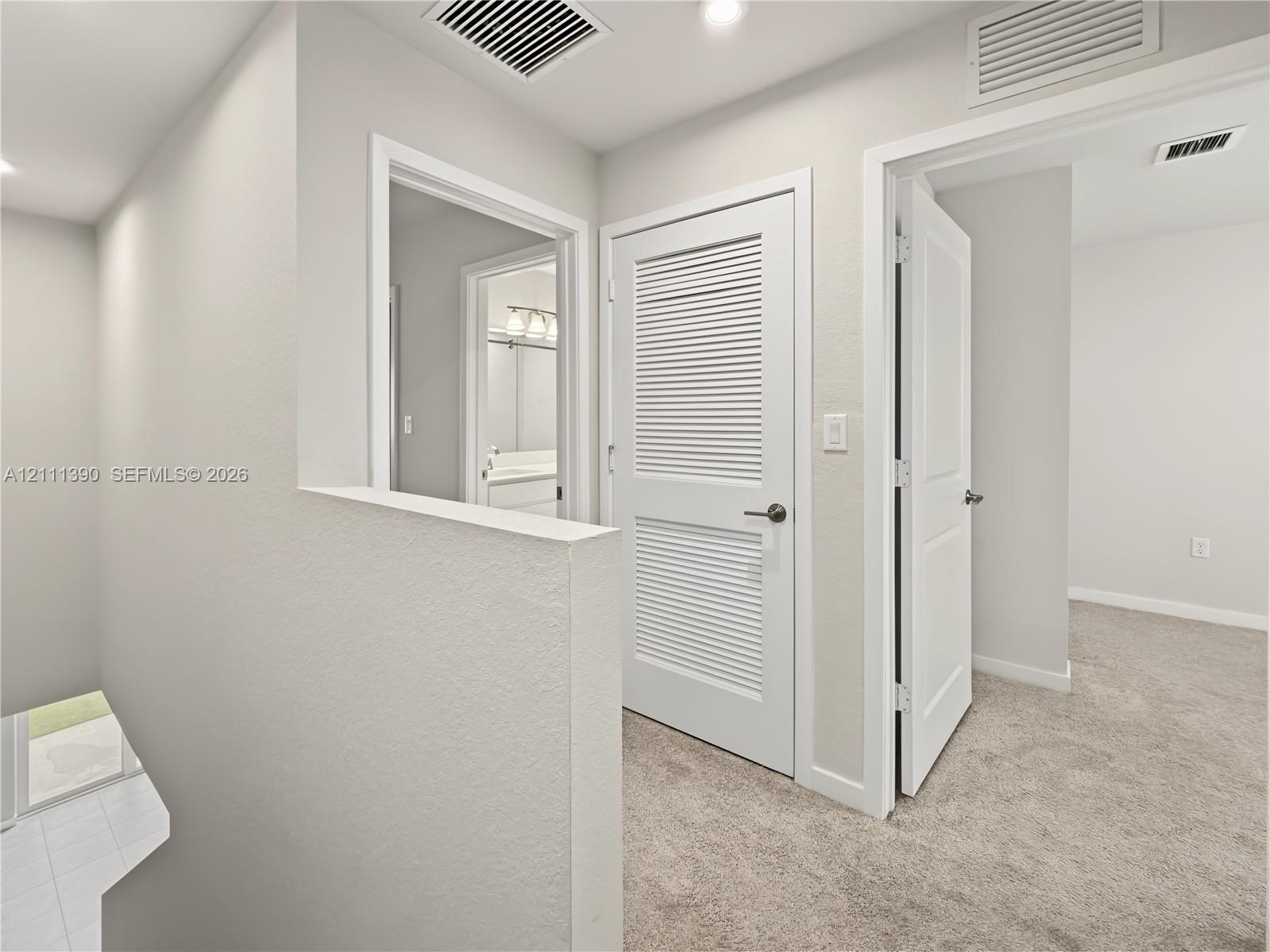Neutral-toned interior featuring wall-to-wall carpeting, white paneled interior doors, and a louvered closet door
