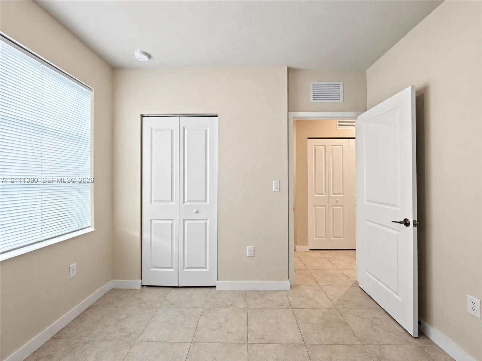 Neutral-toned room featuring tile flooring, a window with horizontal blinds, and two sets of white panel doors