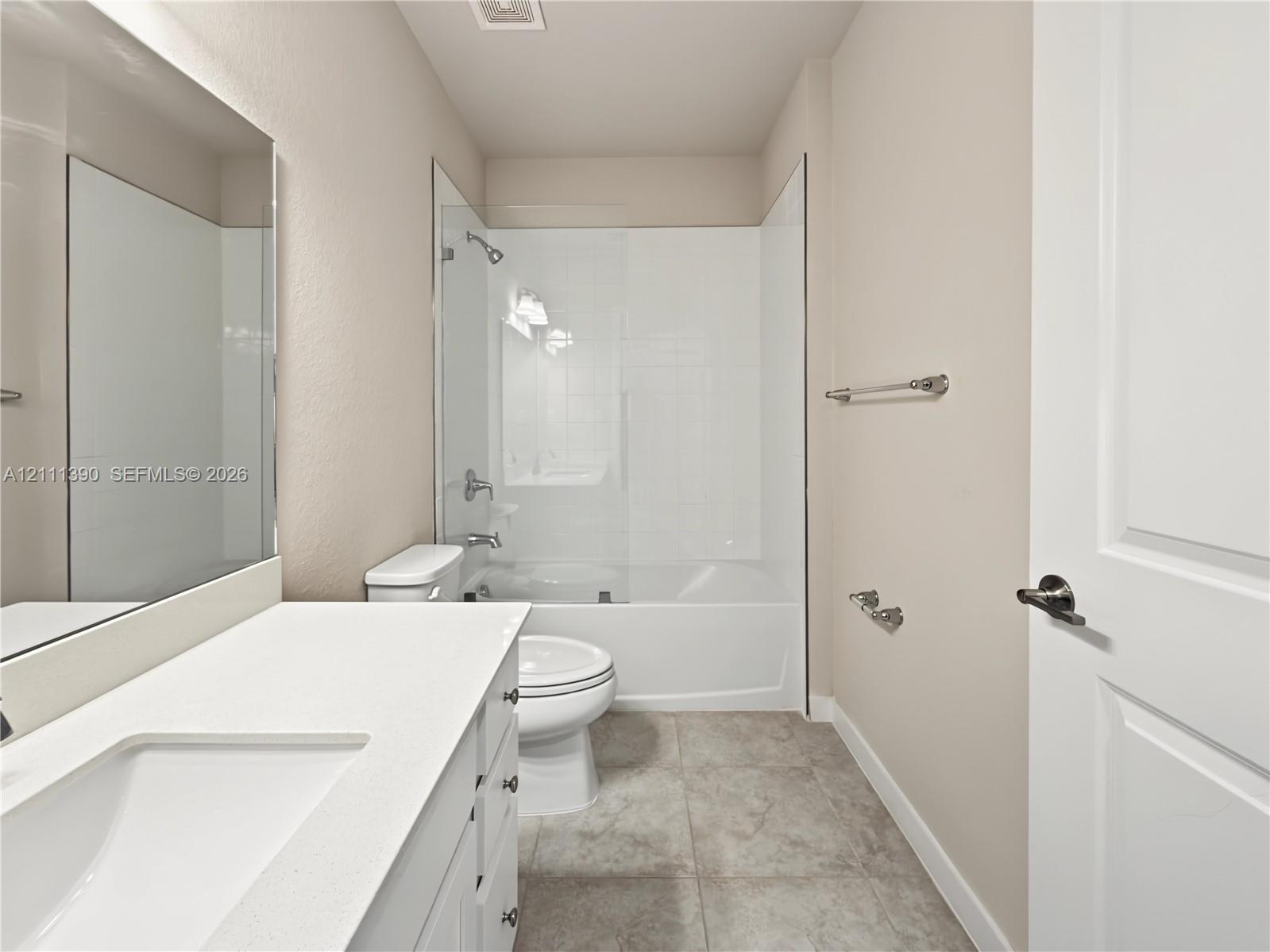 Bathroom featuring a vanity with a white countertop and rectangular undermount sink, a large wall-mounted mirror, tile flooring, and a tub-shower combination with a glass panel