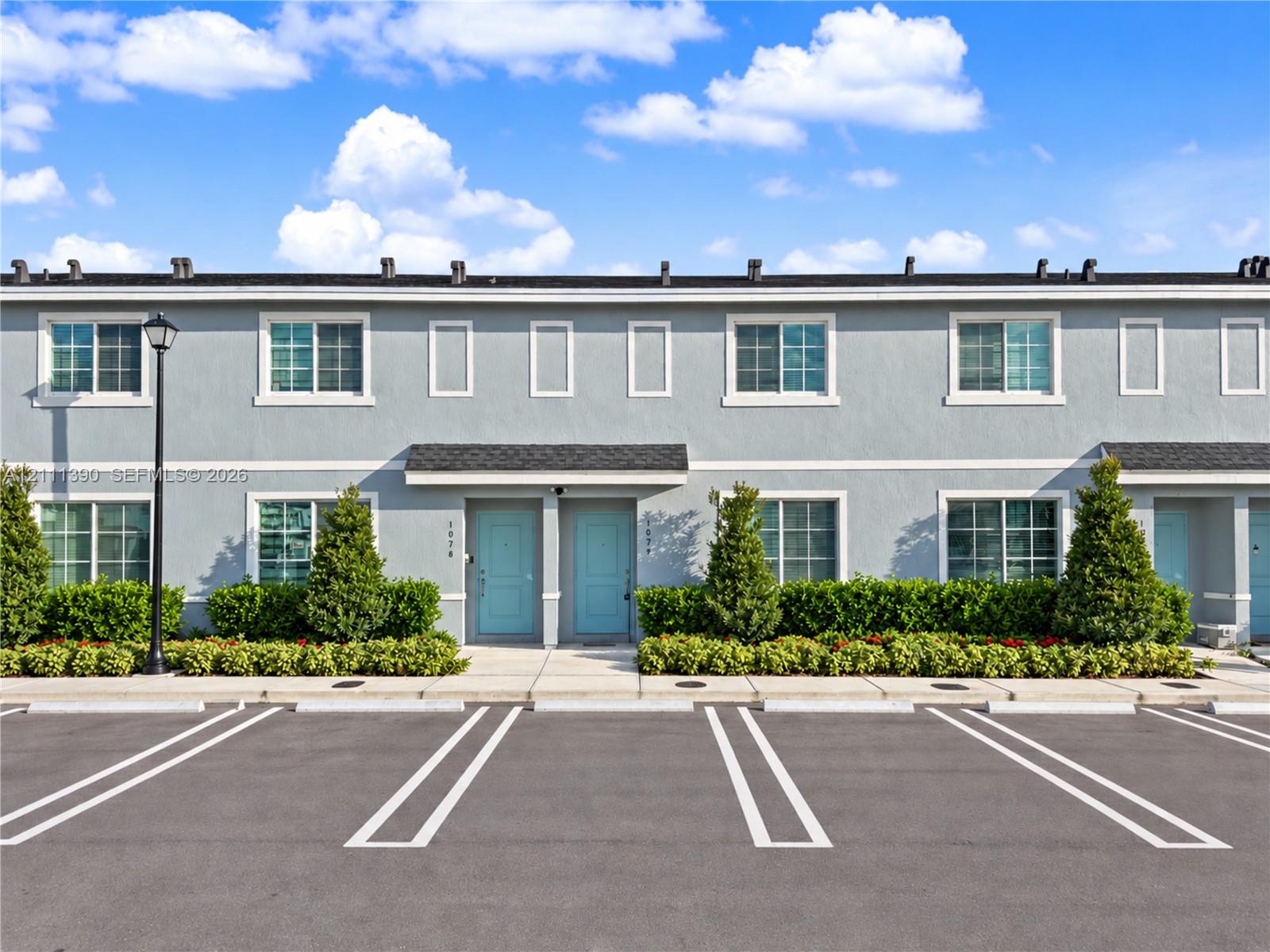Two-story multi-unit exterior featuring smooth grey stucco facade, dark asphalt shingle roof, dual light-blue entry doors, and dedicated paved parking stalls