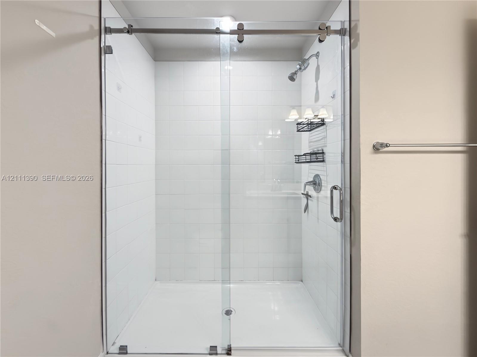 Walk-in shower featuring white subway wall tile, a frameless glass sliding door with brushed metal hardware, and a fixed shower head