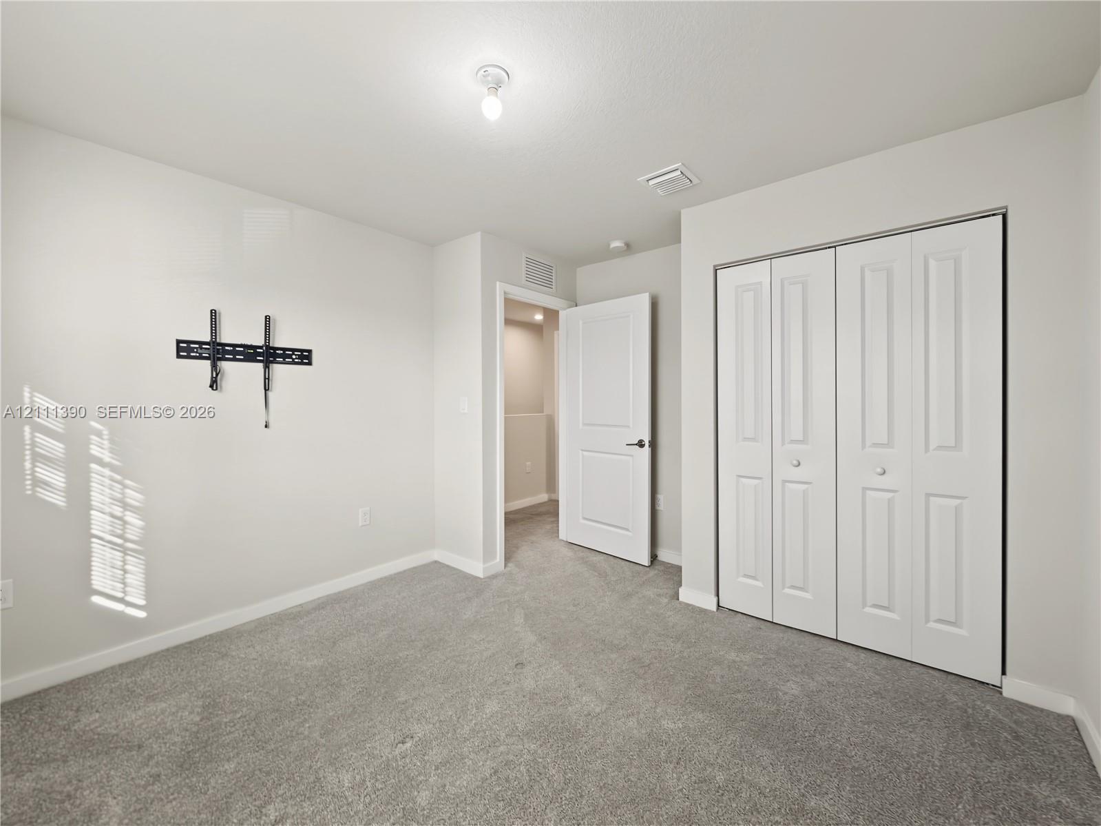 Room featuring neutral-toned carpeting, white walls, two-panel interior door, and white bi-fold closet doors