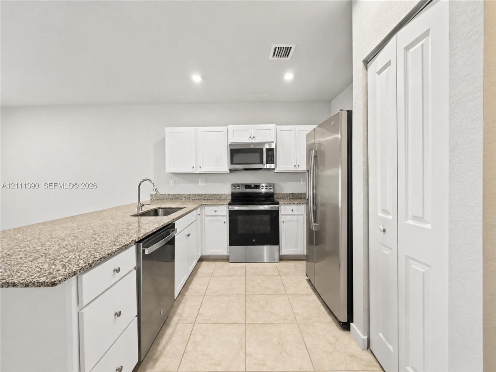 Kitchen featuring white shaker-style cabinetry, stone-finish countertops, stainless steel appliances, ceramic tile flooring, and a double-door pantry