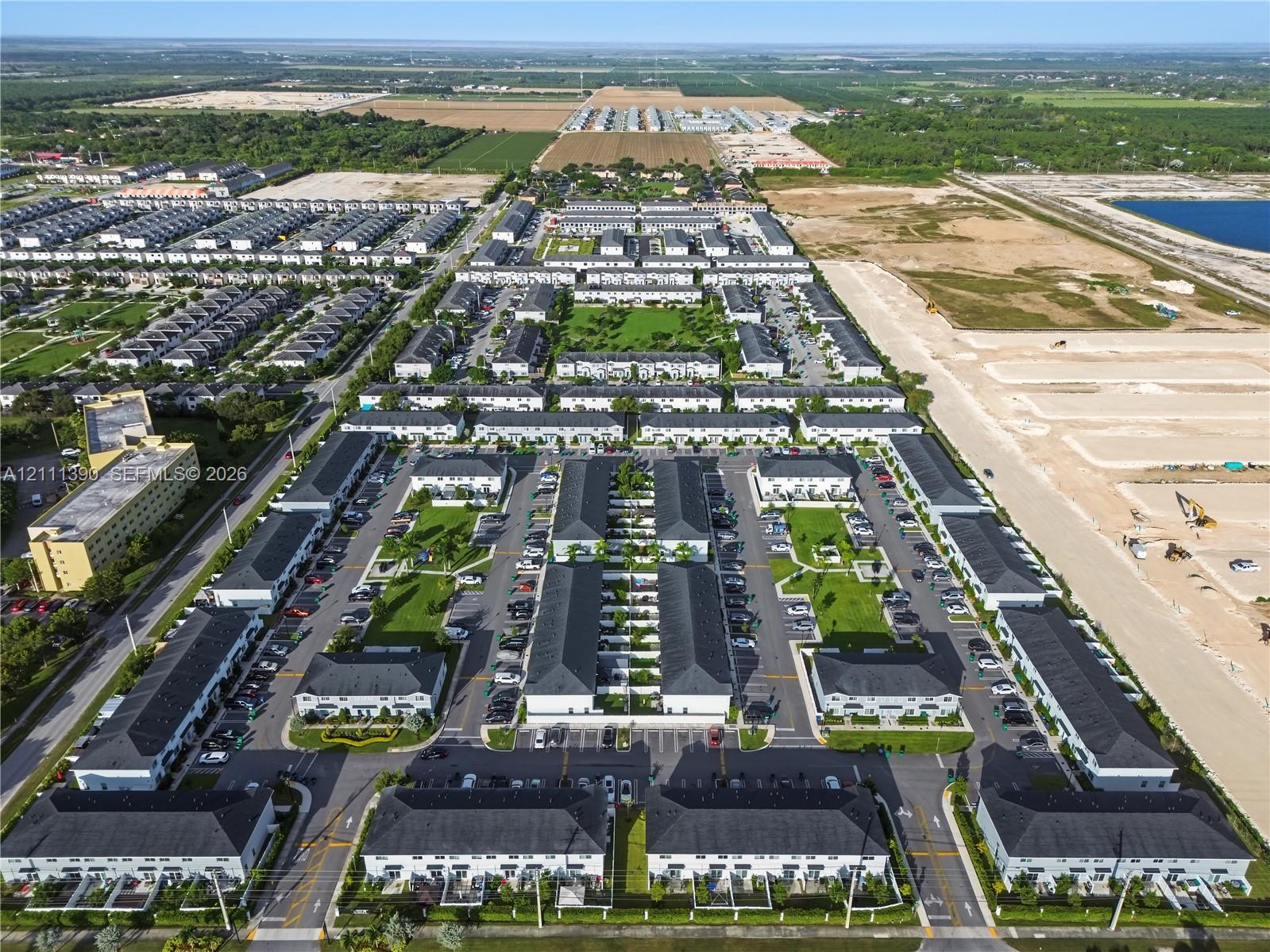Aerial perspective of a multi-unit residential community featuring uniform architectural design, pitched roofs, paved internal roadways, and landscaped common green spaces