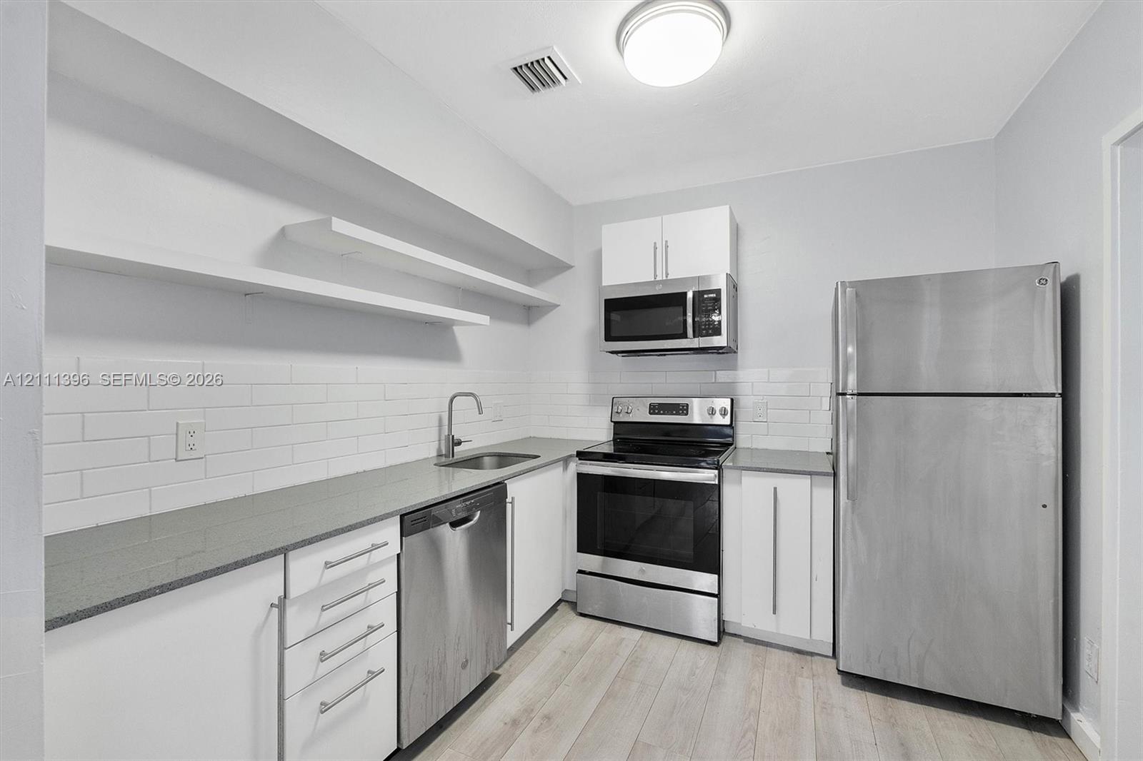 Kitchen featuring white cabinetry, stainless steel appliances, solid-surface countertops, subway tile backsplash, and wood-finish flooring