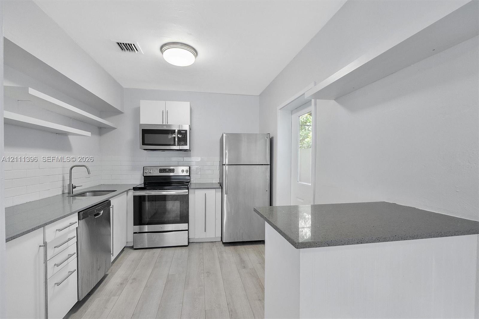 Kitchen featuring white shaker-style cabinetry, quartz countertops, stainless steel appliances, white subway tile backsplash, and light-toned wood-finish flooring