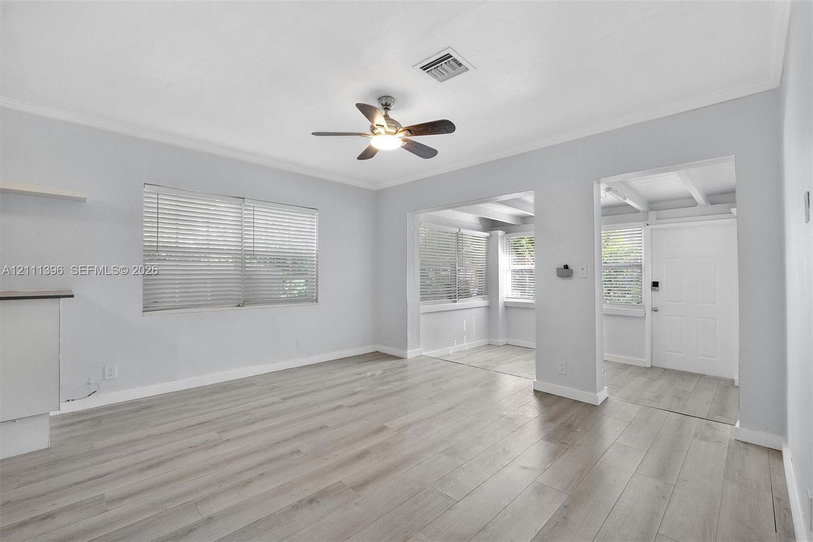 Interior space featuring neutral wall paint, wood-finish flooring, a ceiling fan with integrated lighting, and multiple windows with horizontal blinds