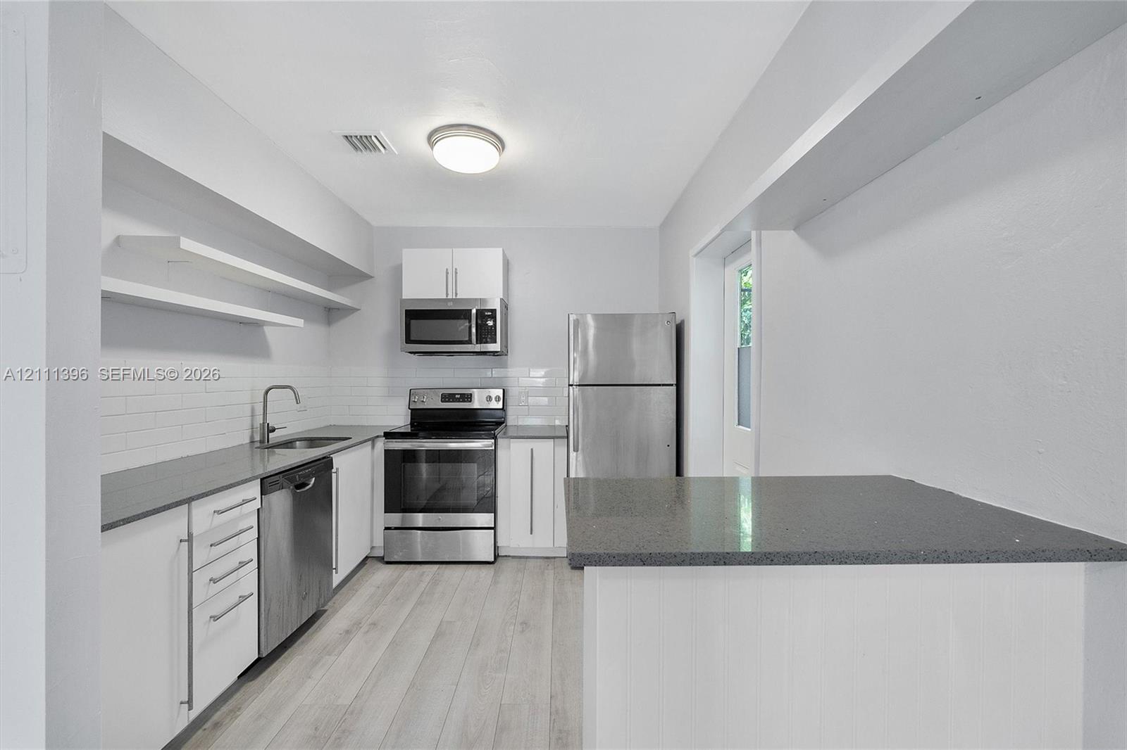 Kitchen featuring white cabinetry, solid-surface countertops, subway tile backsplash, stainless steel appliances, and wood-finish flooring