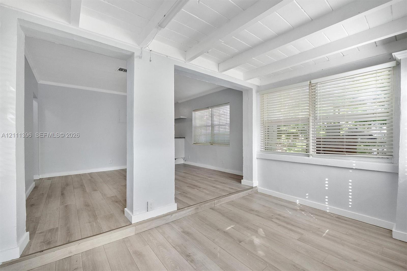Exposed wood-beam ceiling, wood-finish flooring, and large windows with horizontal blinds