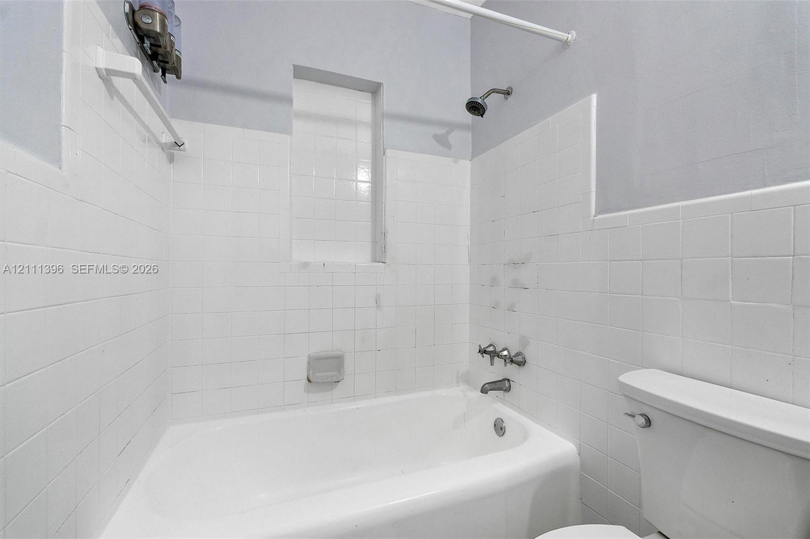 Bathroom featuring a white porcelain tub, ceramic wall tiling, a built-in recessed shelf, and a dual-handle metal faucet