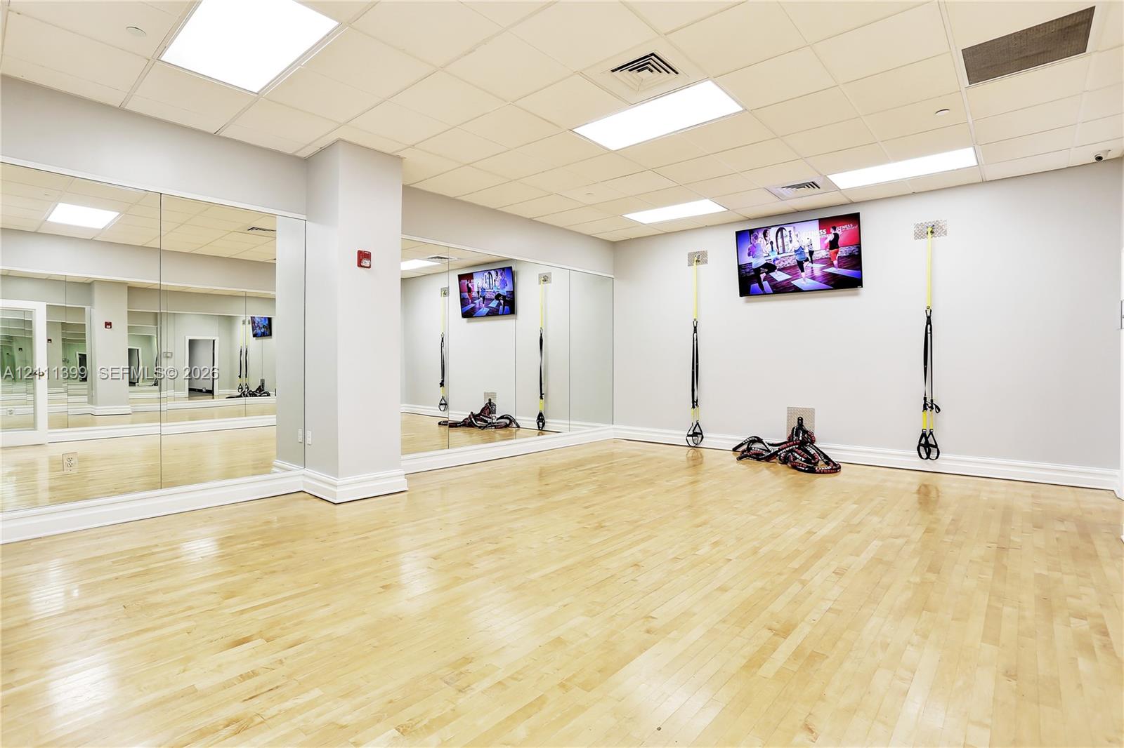 Fitness area featuring wood-finish flooring, full-length wall mirrors, recessed panel lighting, and wall-mounted television screens