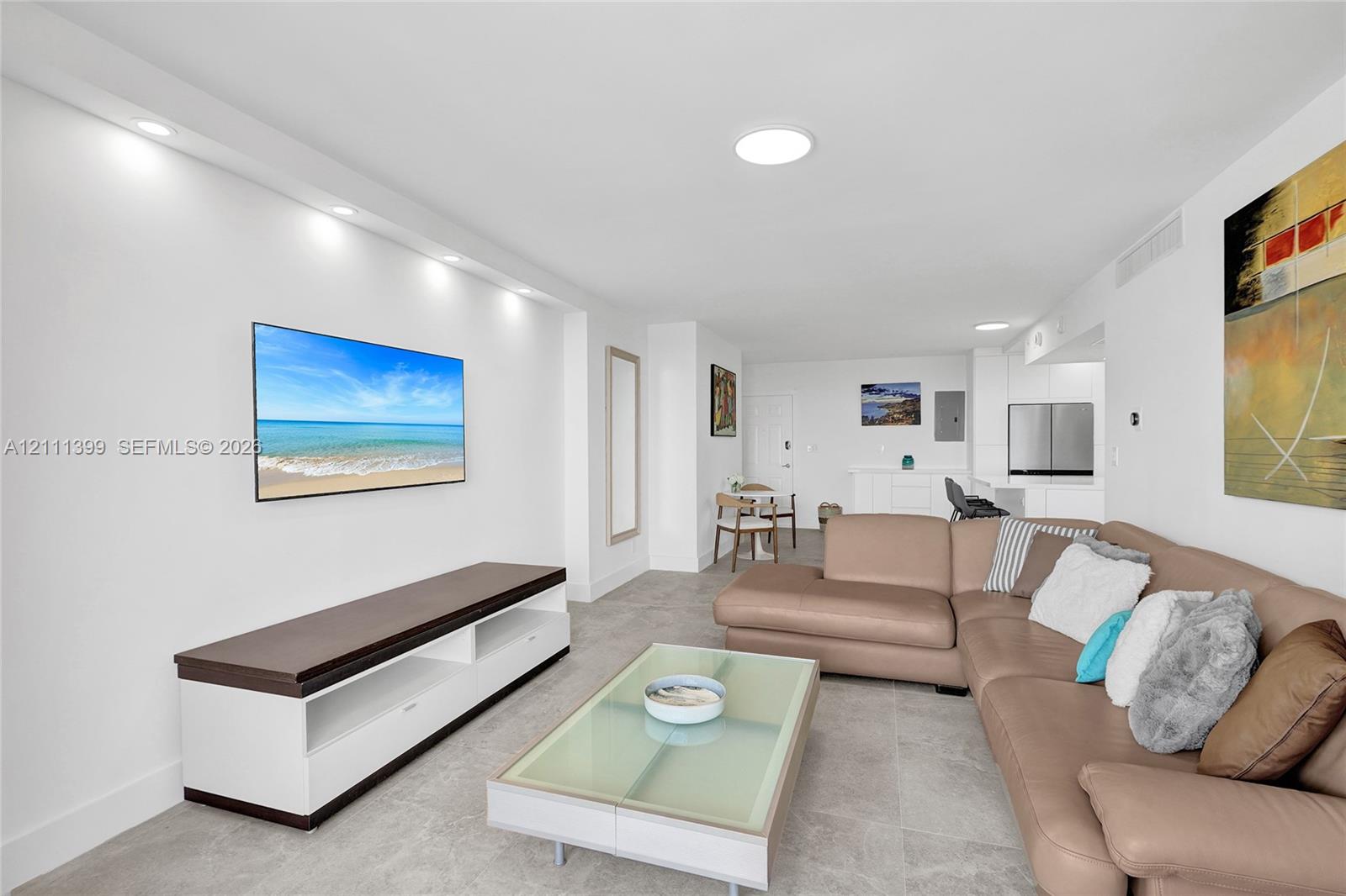 Open-concept living area featuring light-toned tile flooring, recessed ceiling lighting, and a custom built-in media console with storage