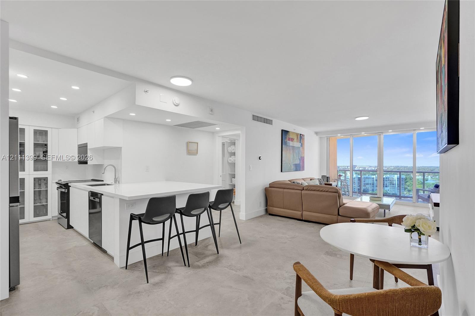 Living area featuring tile flooring, recessed ceiling lighting, and floor-to-ceiling glass sliding doors opening to a balcony with metal railings