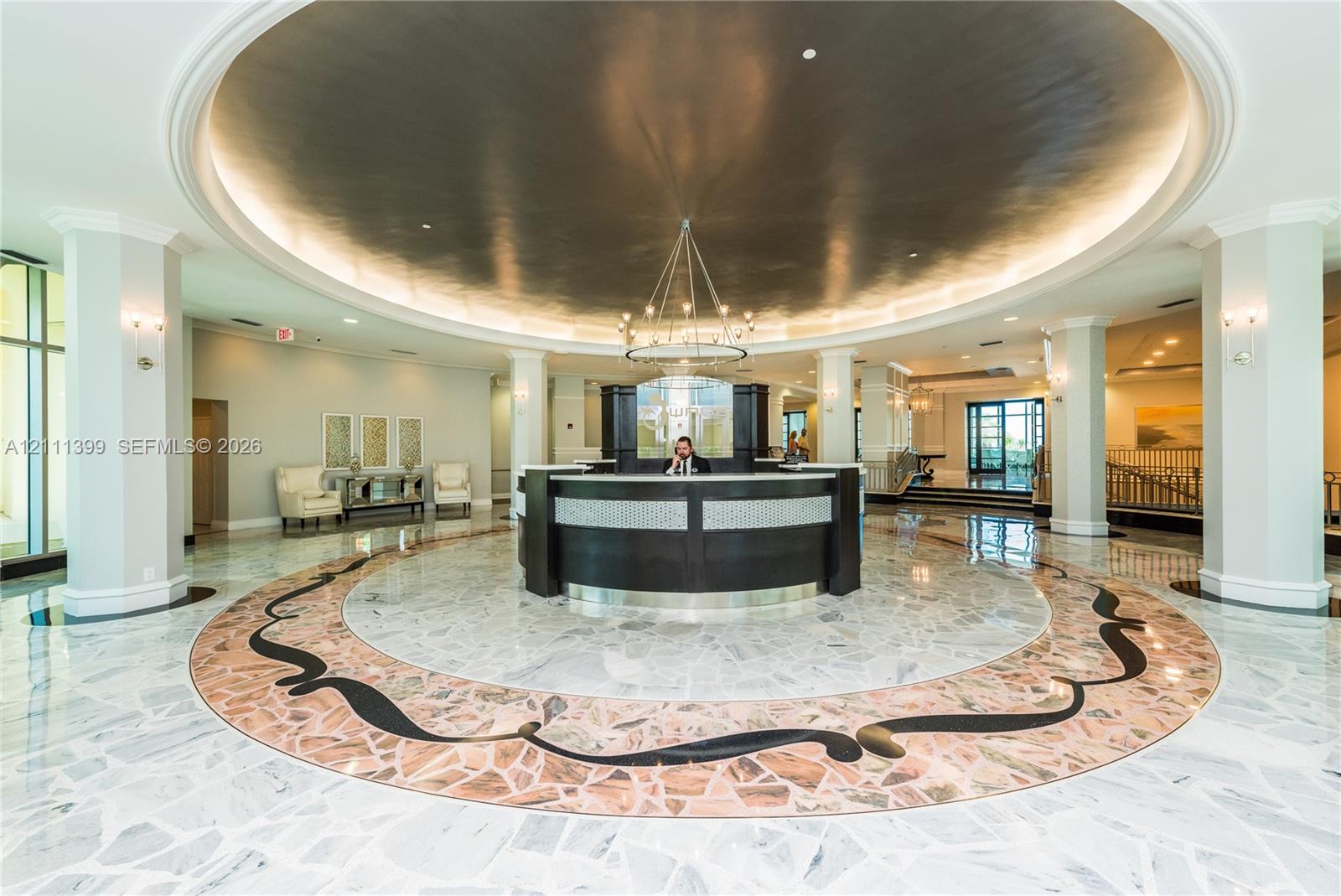 Grand foyer featuring a circular stone tile floor with decorative inlay, a coffered domed ceiling with recessed lighting, structural support columns, and a built-in reception desk