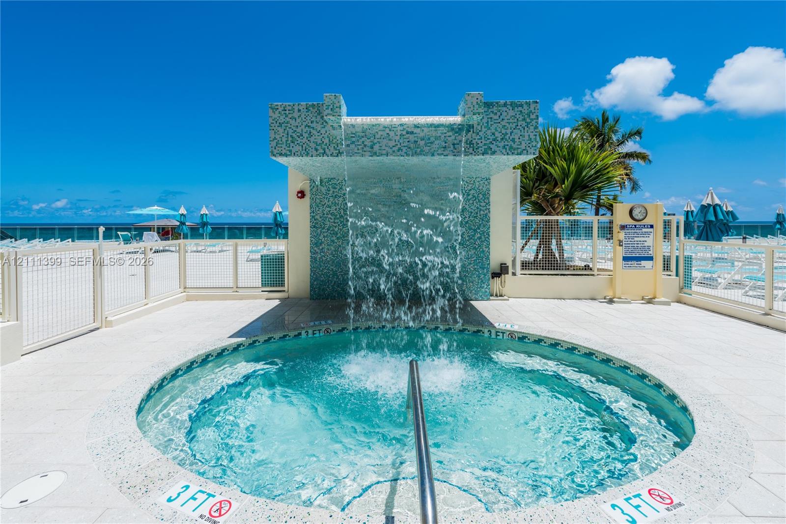 Circular spa featuring a decorative tile waterfall feature and white stone-finish decking