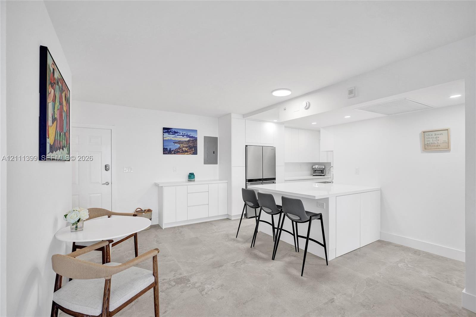 Modern kitchen featuring a central island with integrated storage, flat-panel cabinetry, light-toned stone-finish countertops, stainless steel appliances, and large-format tile flooring
