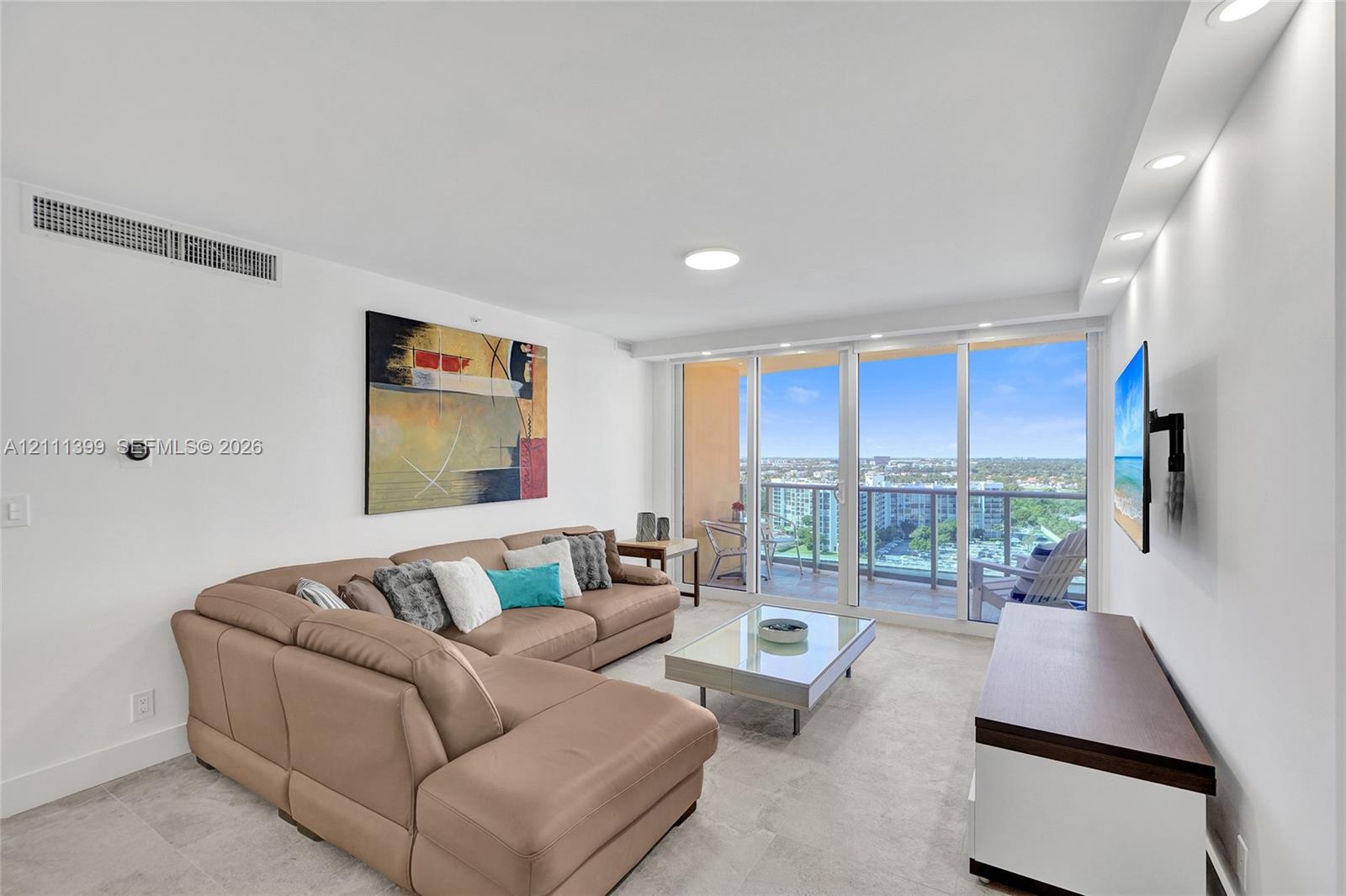 Living area featuring tile flooring, recessed ceiling lighting, and floor-to-ceiling glass sliding doors opening to a balcony with metal railings