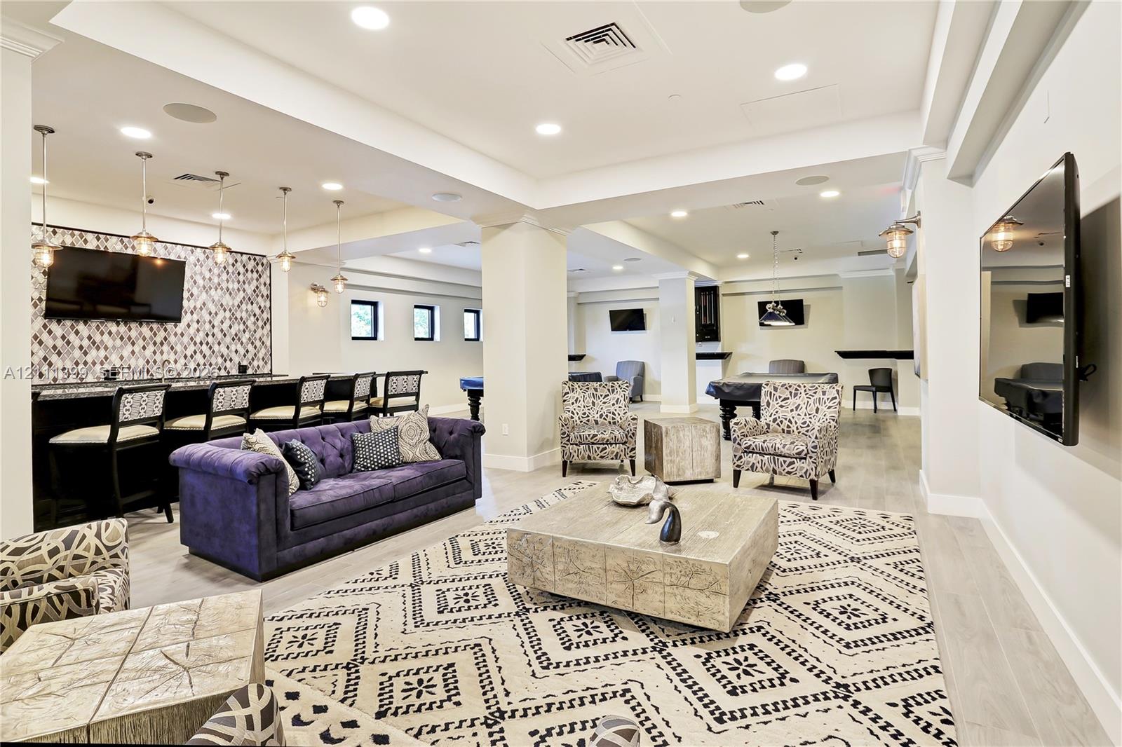Open-concept common area featuring recessed lighting, light-toned wood-finish flooring, a full wet bar with patterned tile backsplash, and multiple mounted television screens