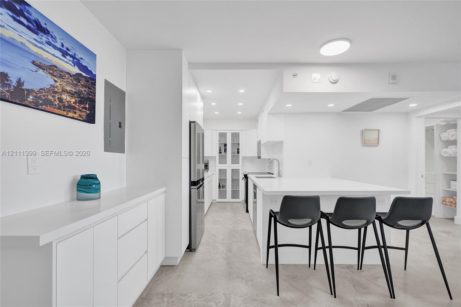Kitchen featuring white flat-panel cabinetry, stone countertops, stainless steel refrigerator, glass-front upper cabinet, and recessed ceiling lighting