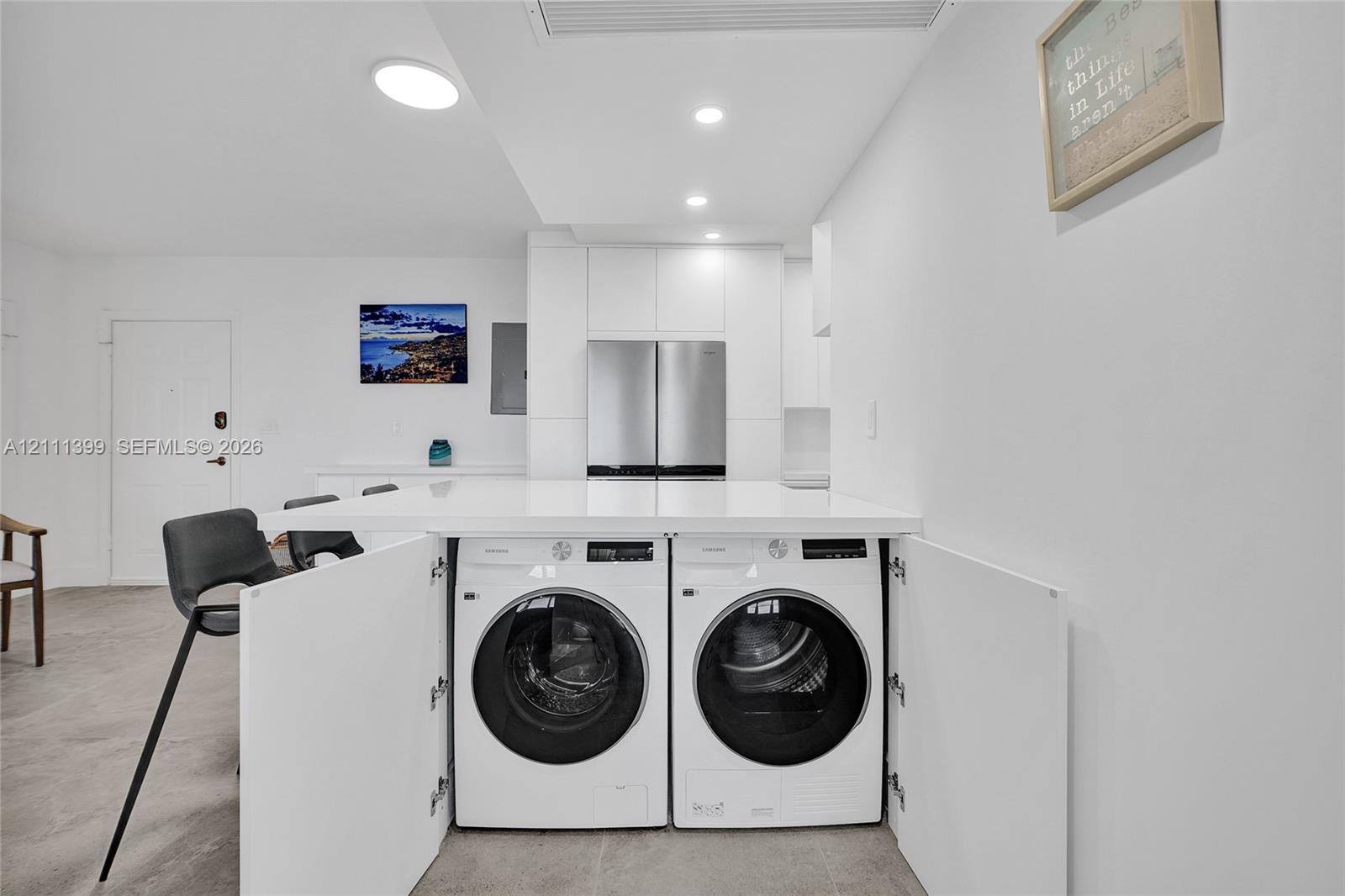 Kitchen featuring white flat-panel cabinetry, stainless steel appliances, solid-surface countertop, and integrated laundry center with built-in cabinetry