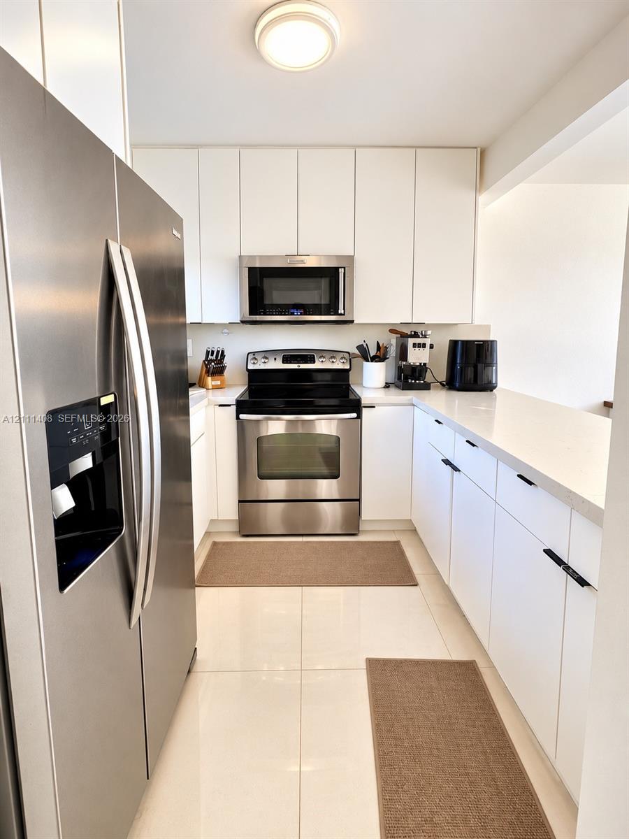 Interior hallway featuring oversized floor tiles, white cabinetry with matte black hardware, and closet doors with louvered panels