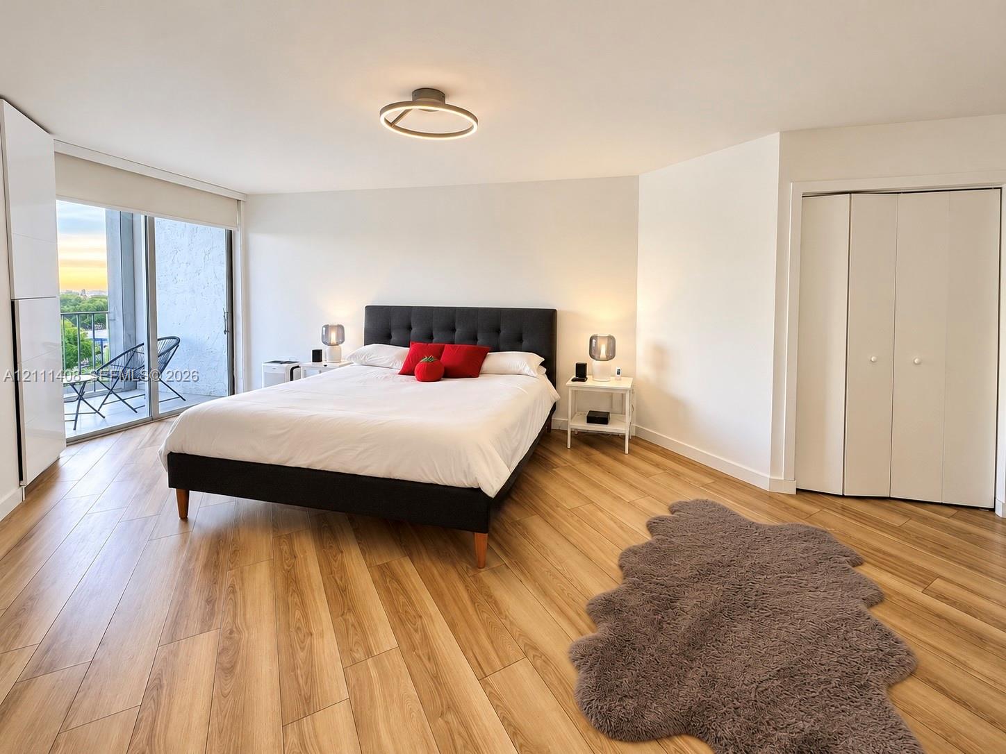 Wood-finish flooring, flush-mount circular lighting, and sliding glass doors leading to a balcony
