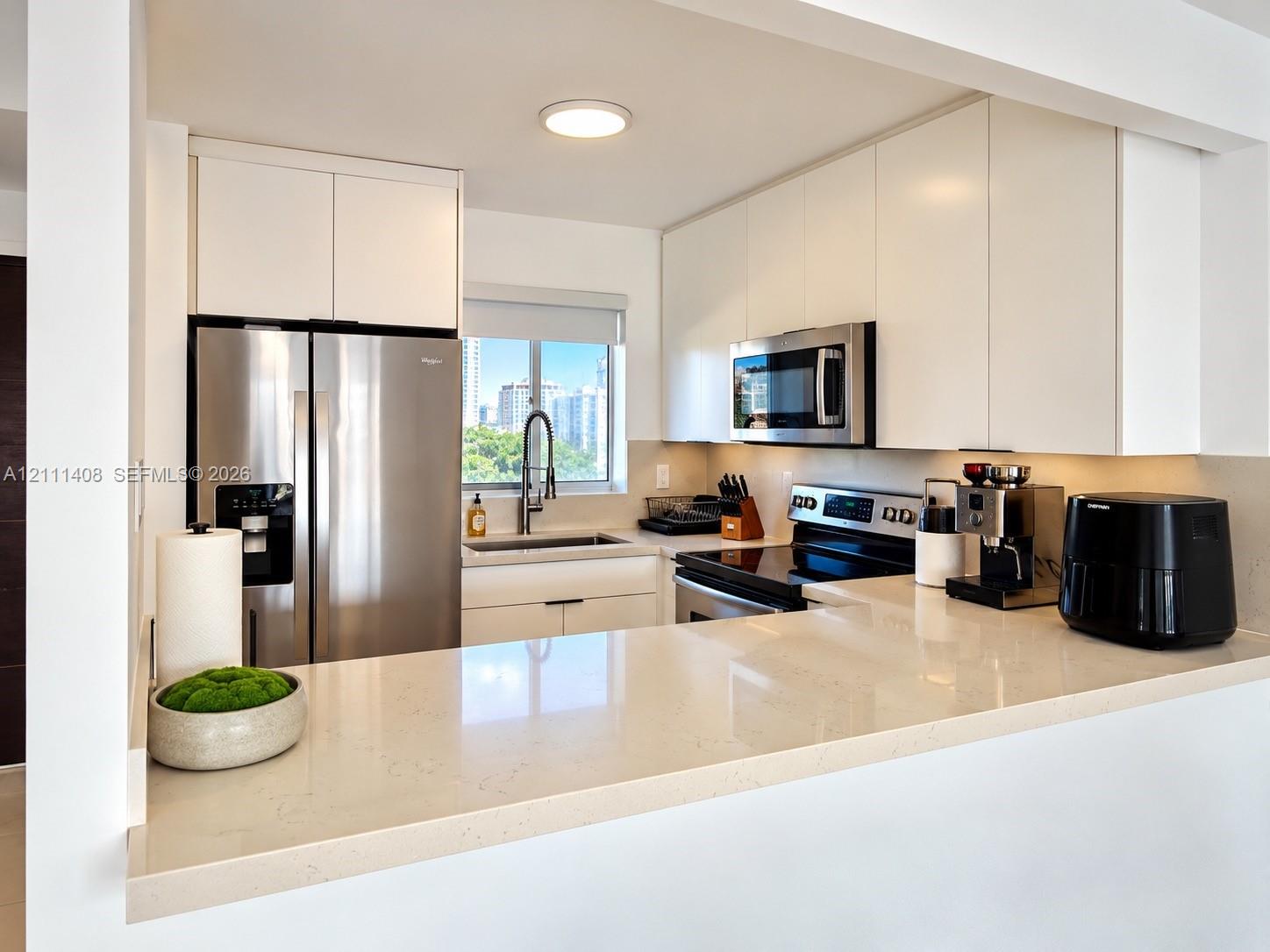 Kitchen featuring white cabinetry, solid-surface countertops, tile flooring, and stainless steel appliances including a built-in microwave and refrigerator