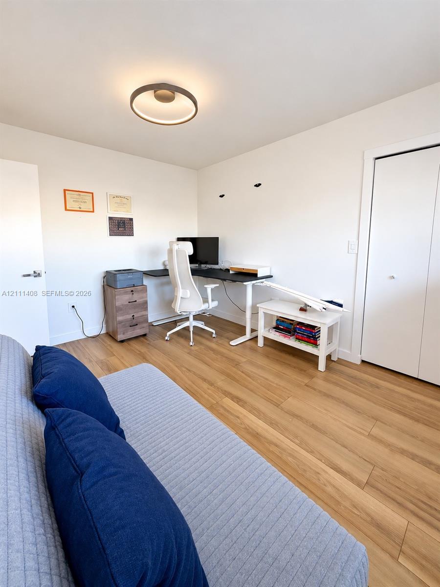 Interior room featuring light-toned wood-finish flooring, a contemporary flush-mount ceiling light fixture, and a solid-core interior door with matte black hardware
